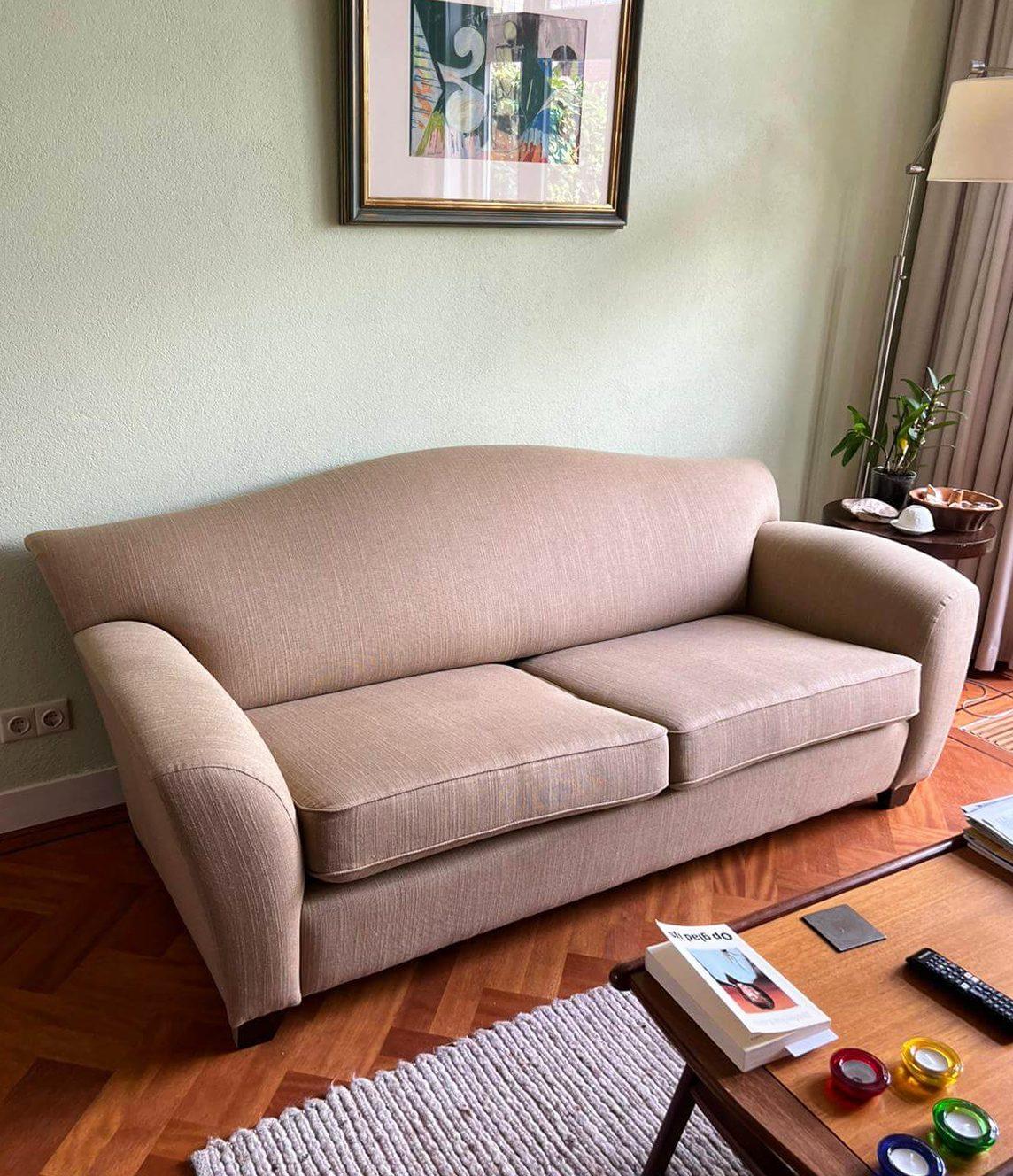 Beige bank met twee zitkussens in een woonkamer met een houten vloer