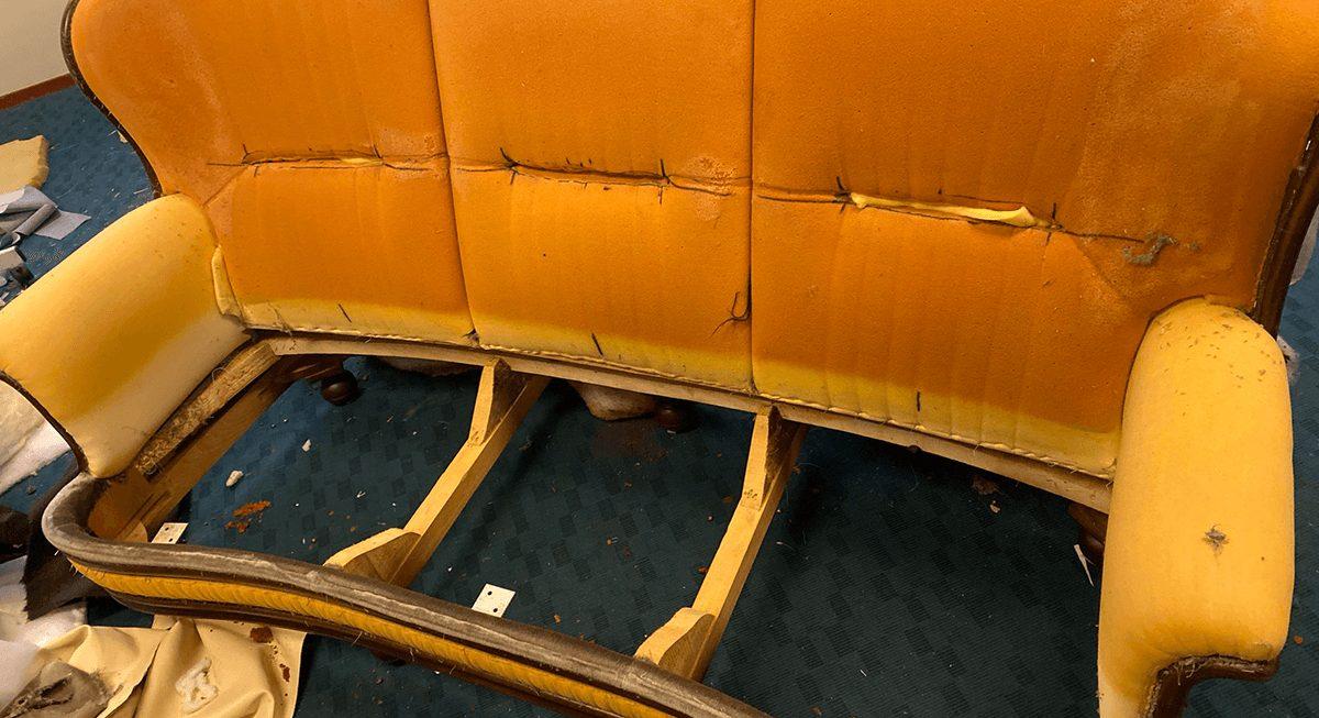 Gebogen bank zonder zitting, met oranje en gele bekleding op de rug en de armleuningen