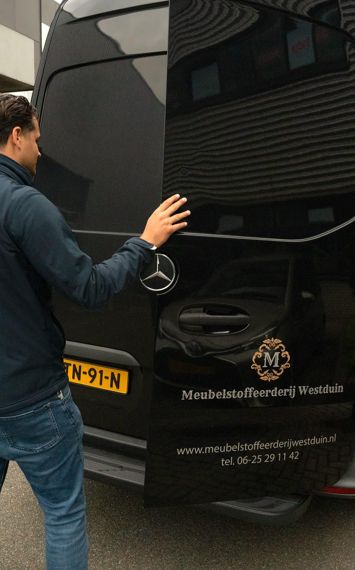 Medewerker bij de achterdeur van de bedrijfsbus met het logo van Meubelstoffeerderij Westduin