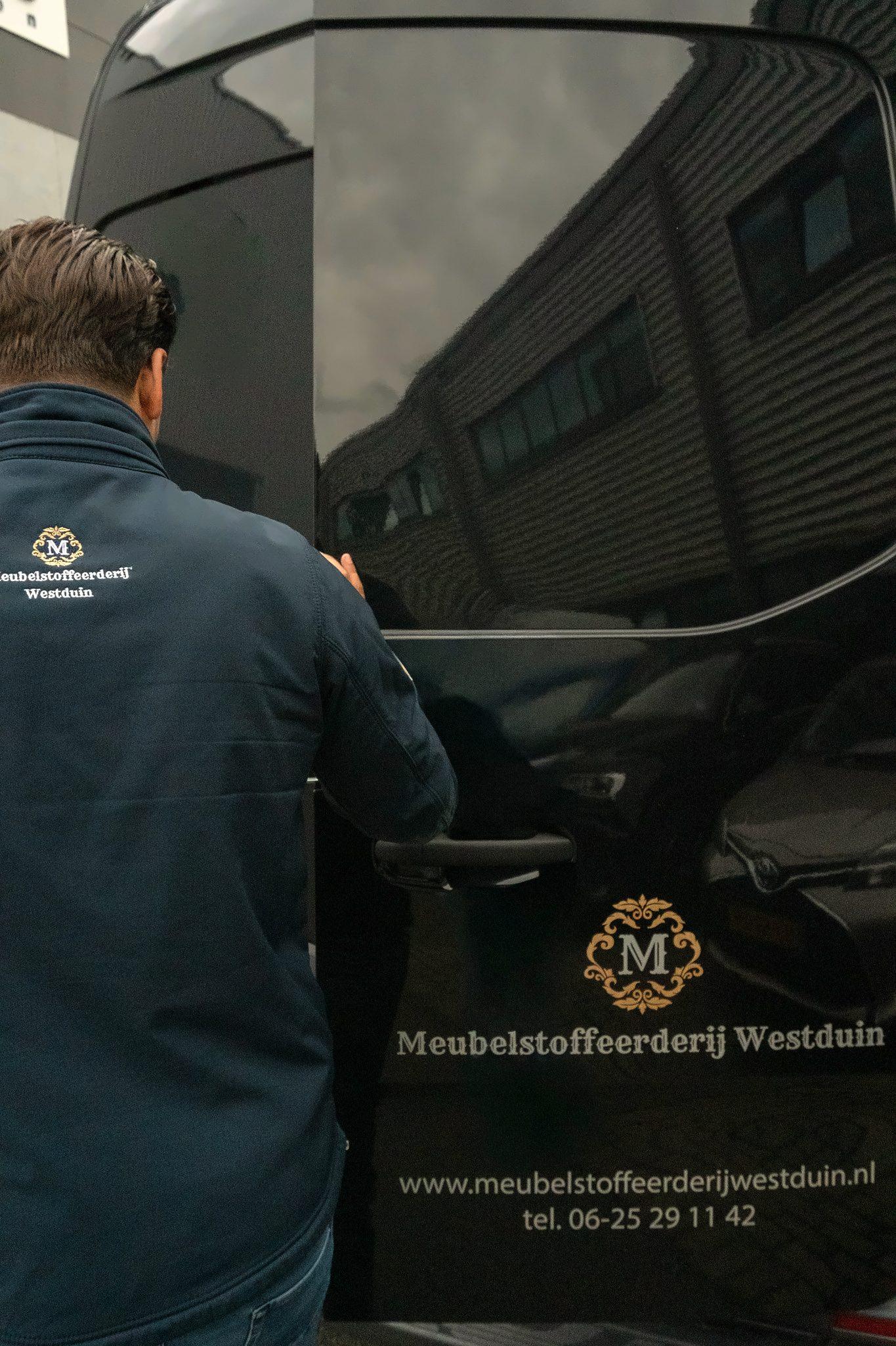 Medewerker opent de achterdeur van de bedrijfsbus met het logo, de website en het telefoonnummer