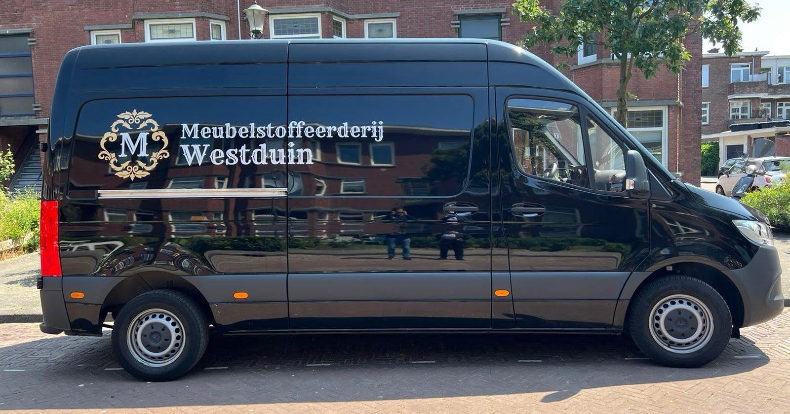 Zwarte bedrijfsbus met het logo en de naam Meubelstoffeerderij Westduin op de zijkant