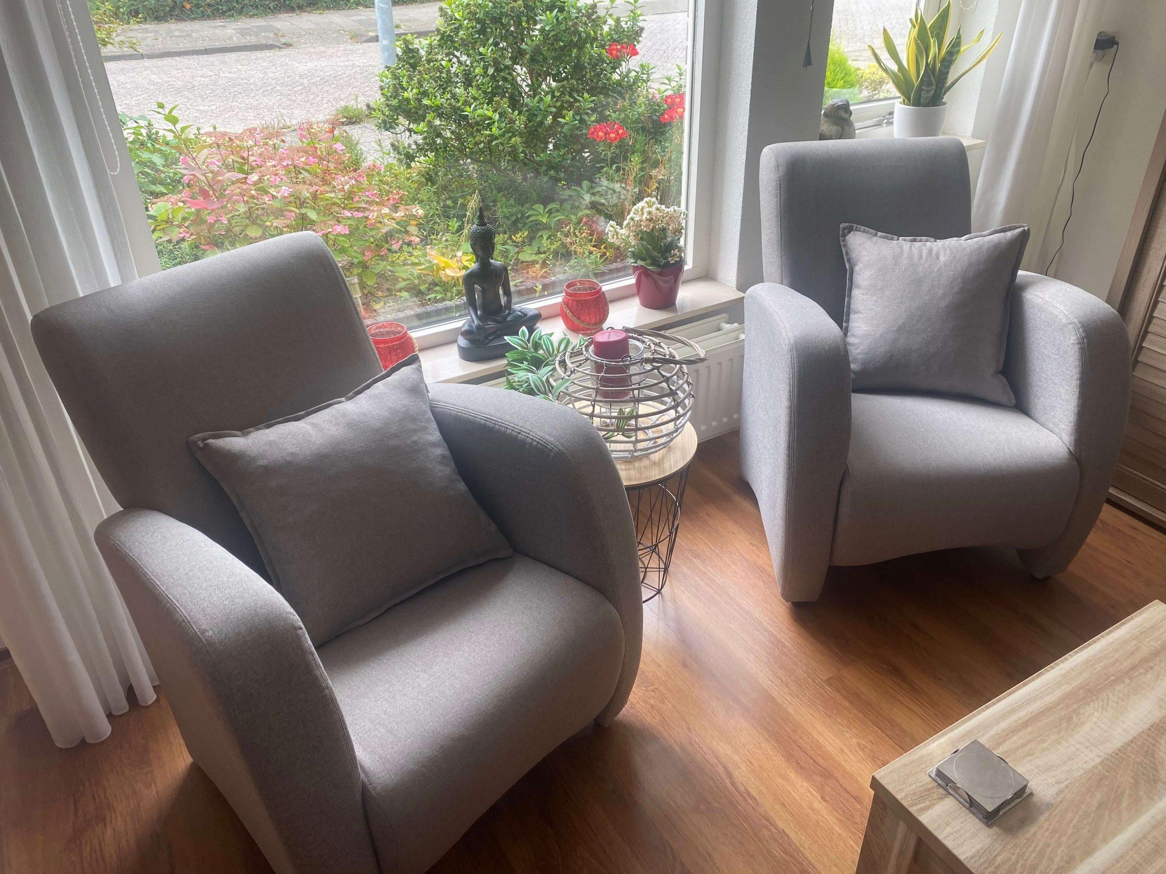 Twee grijze fauteuils met sierkussens bij een raam