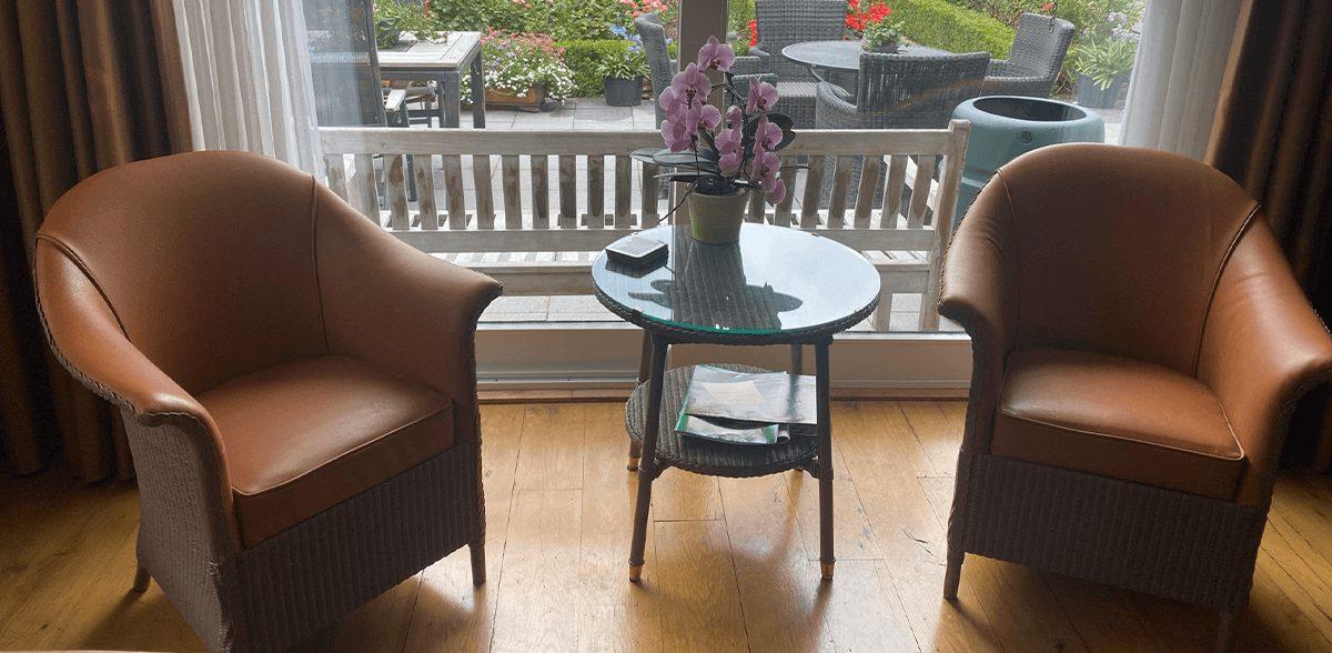Twee rieten fauteuils met cognackleurig leer aan de binnenkant, bij een raam