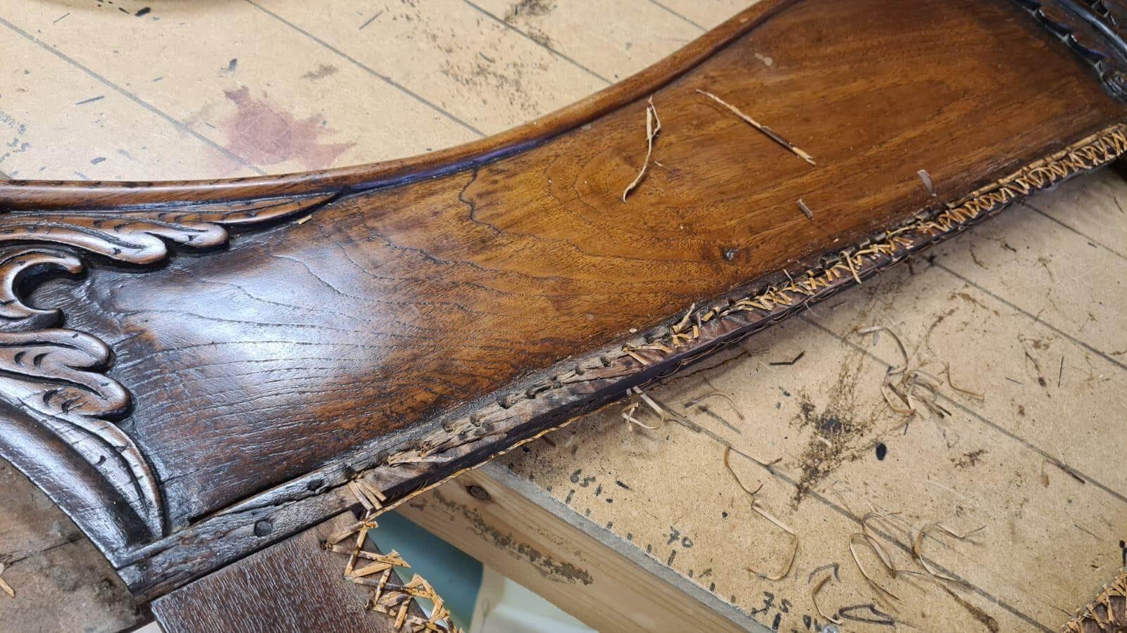 Houten armleuning met resten van oud riet langs de rand