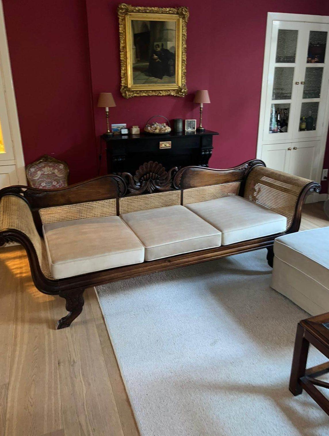 Rietbank met drie lichte zitkussens in een woonkamer met een rode wand