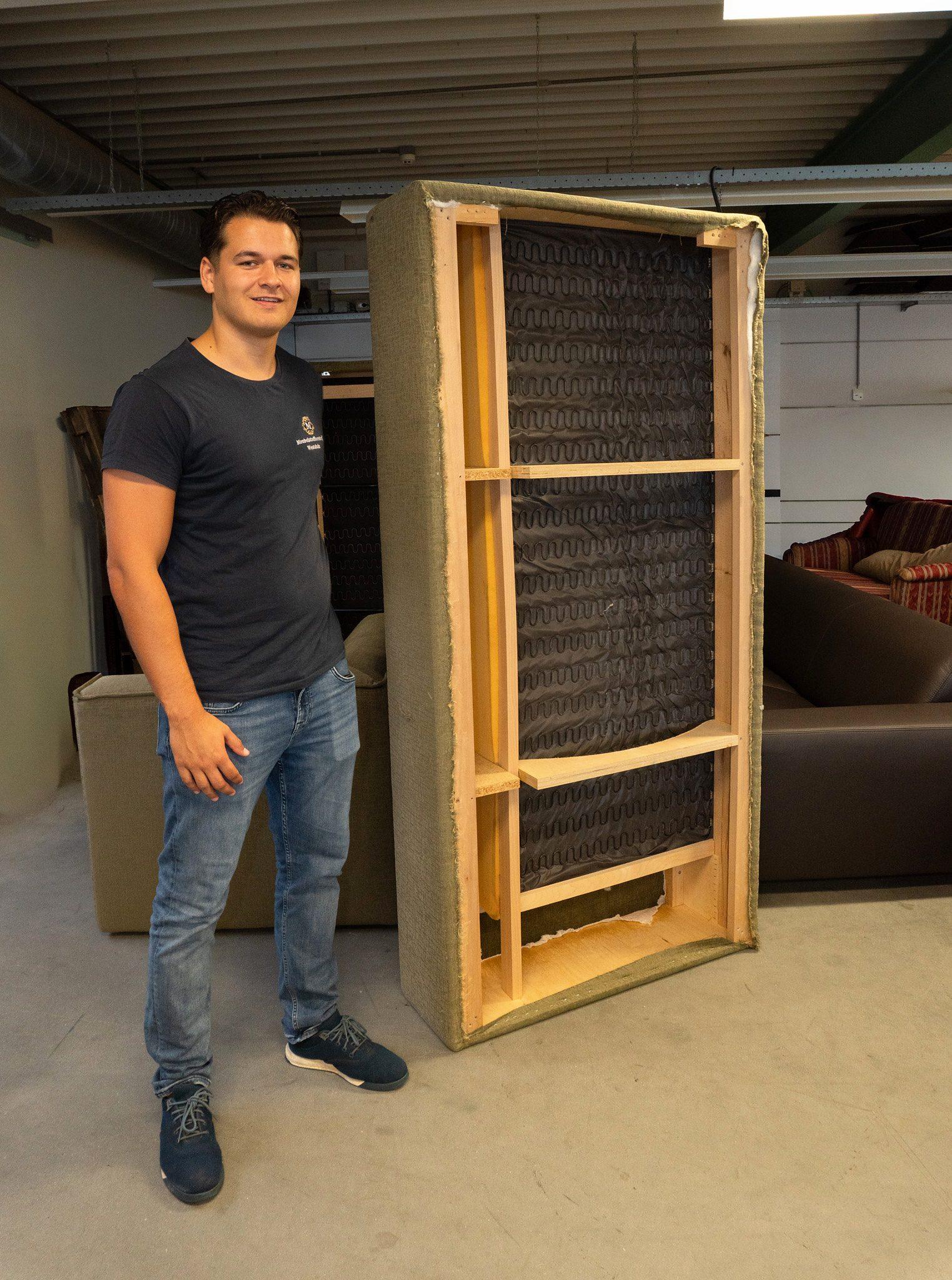 Medewerker van Meubelstoffeerderij Westduin in de werkplaats, naast een rechtopstaand houten frame met veren