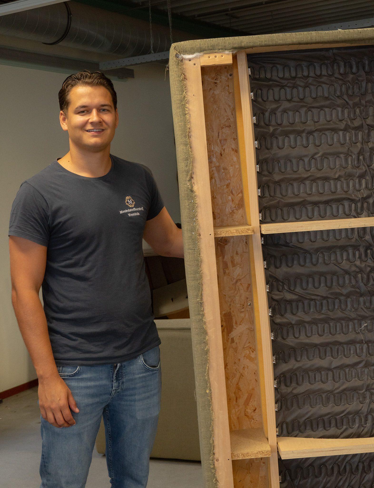 Medewerker van Meubelstoffeerderij Westduin in de werkplaats, naast een houten frame met veren
